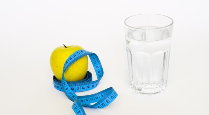 GLP-1 Programs in New York City Yellow apple with a blue measuring tape wrapped around it, next to a glass of water on a white background — health and diet theme