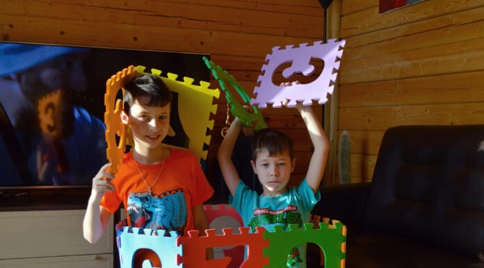 Best Toys for Autistic Children Two kids stand inside a bright, multicolor foam block play structure with interlocking letter panels in a wood-paneled room.
